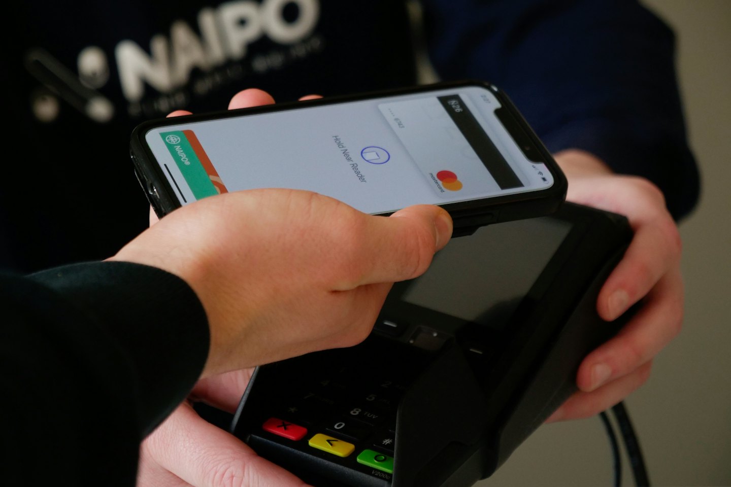 Hands making contactless payment with a smartphone at a terminal.